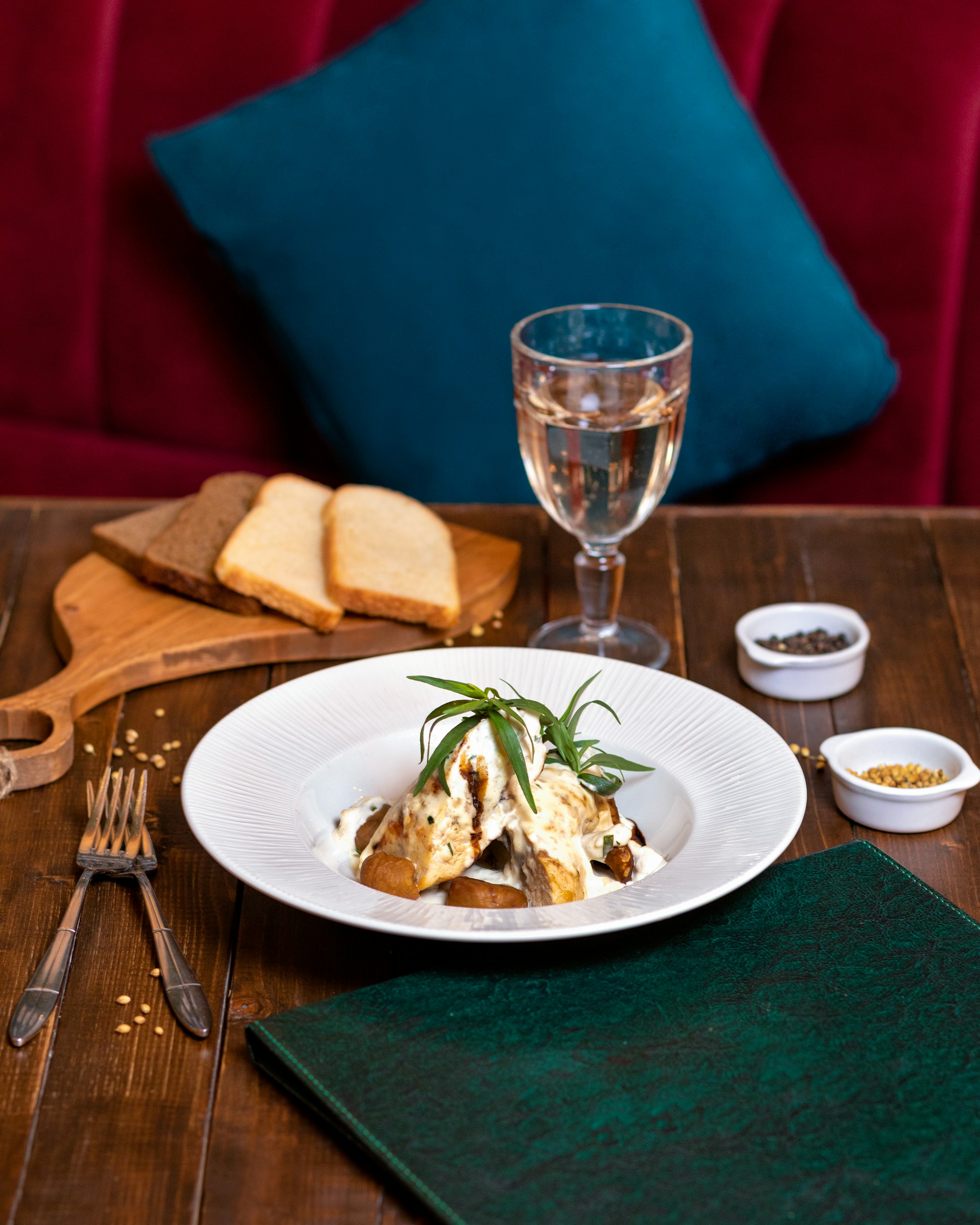 A close-up of a beautifully plated international comfort dish, garnished with fresh herbs, served on a wooden table with copper utensils and a coral red linen.