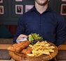 man in blue dress shirt holding brown wooden tray with fries