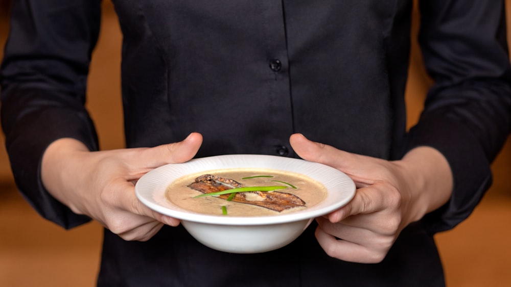 person holding white ceramic bowl with soup