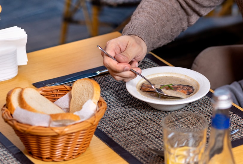 pessoa de suéter cinza tomando sopa em uma tigela de cerâmica branca