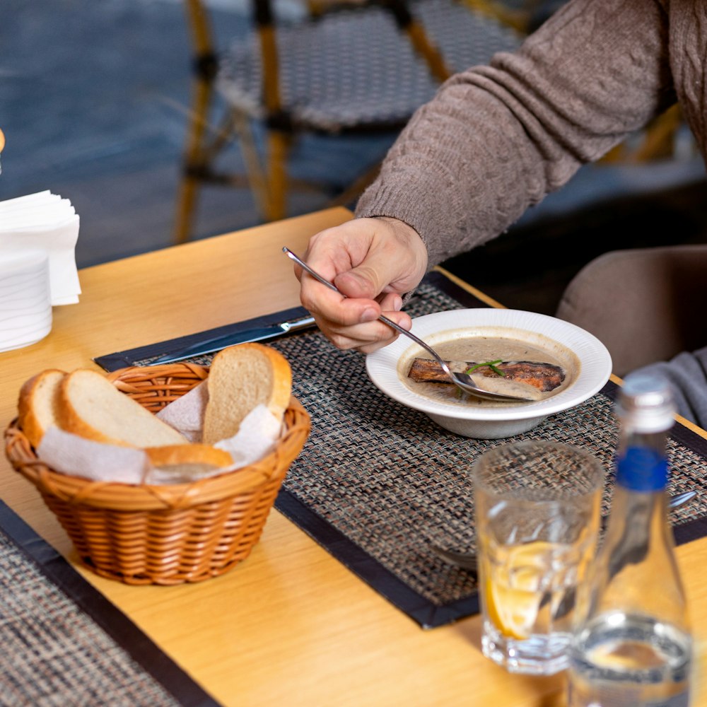 person in gray sweater holding white ceramic bowl with soup