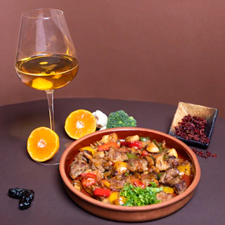 Close-up of a ruby red wine glass beside a plate of herb-roasted chicken with golden vegetables