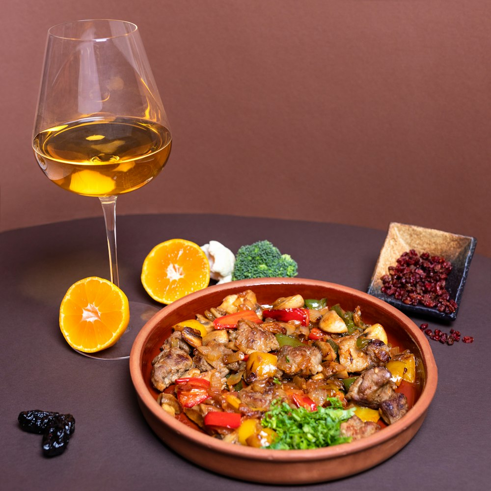 Ensalada de verduras en un cuenco de cerámica marrón junto a una copa de vino transparente