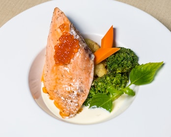 A close-up of a grilled salmon fillet served with steamed broccoli and lemon wedges.