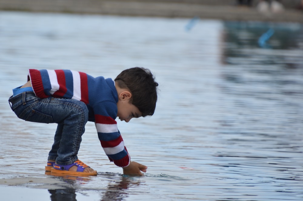 boy in red and blue striped shirt and gray pants sitting on yellow kayak on water