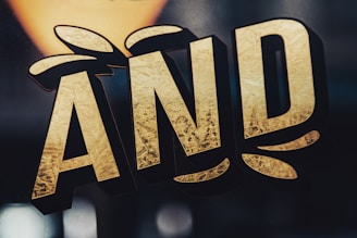 Stylized text in bold, gold letters with a textured surface effect. The letters are outlined in black and appear three-dimensional against a dark background.