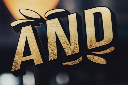 Stylized text in bold, gold letters with a textured surface effect. The letters are outlined in black and appear three-dimensional against a dark background.