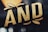 Stylized text in bold, gold letters with a textured surface effect. The letters are outlined in black and appear three-dimensional against a dark background.