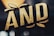 Stylized text in bold, gold letters with a textured surface effect. The letters are outlined in black and appear three-dimensional against a dark background.