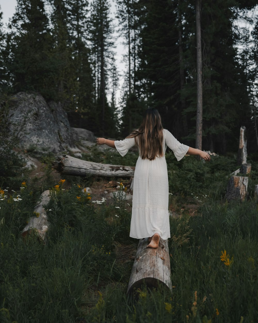 woman in white dress standing on brown tree log during daytime