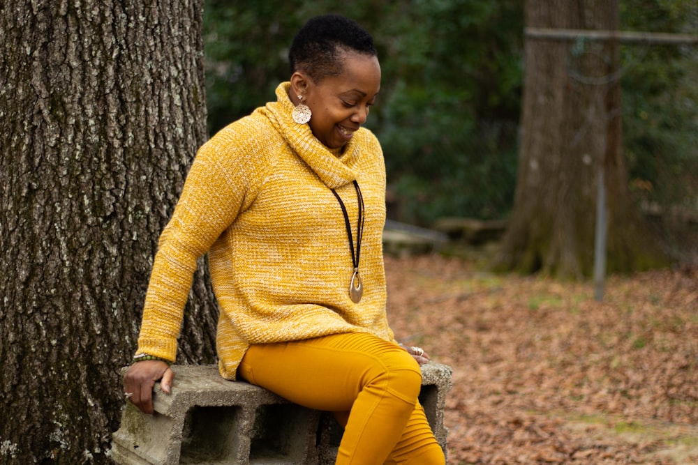黄色いタートルネックのセーターと黄色いズボンを着た女性が灰色のコンクリートのベンチに座っている