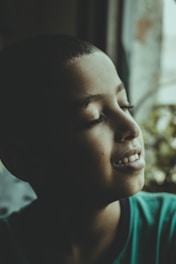 A peaceful young adult sitting calmly by a window with soft natural light.