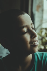 A peaceful young adult sitting calmly by a window with soft natural light.