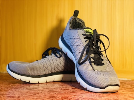 A pair of grey athletic shoes on a wooden surface.