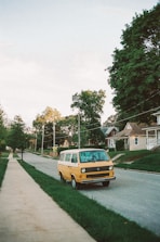 yellow van parked on green grass field near houses and trees during daytime
