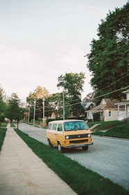 yellow van parked on green grass field near houses and trees during daytime