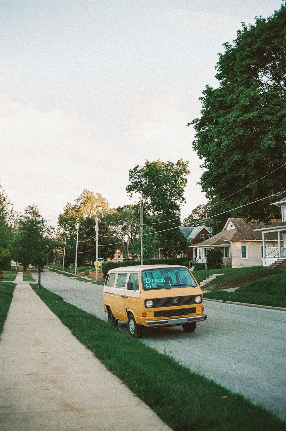 yellow van parked on green grass field near houses and trees during daytime