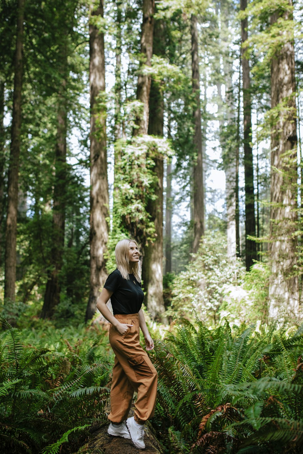 woman in black t-shirt and brown pants standing on green grass field surrounded by trees