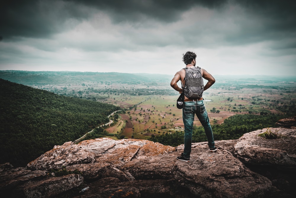 man in black t-shirt and blue denim jeans standing on brown rock during daytime