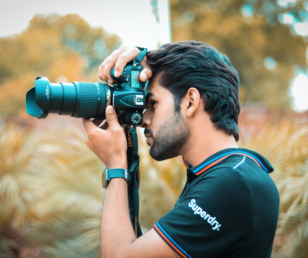 man in blue and orange tank top holding black dslr camera