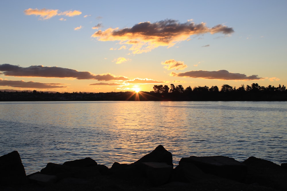 silhouette of rocks near body of water during sunset