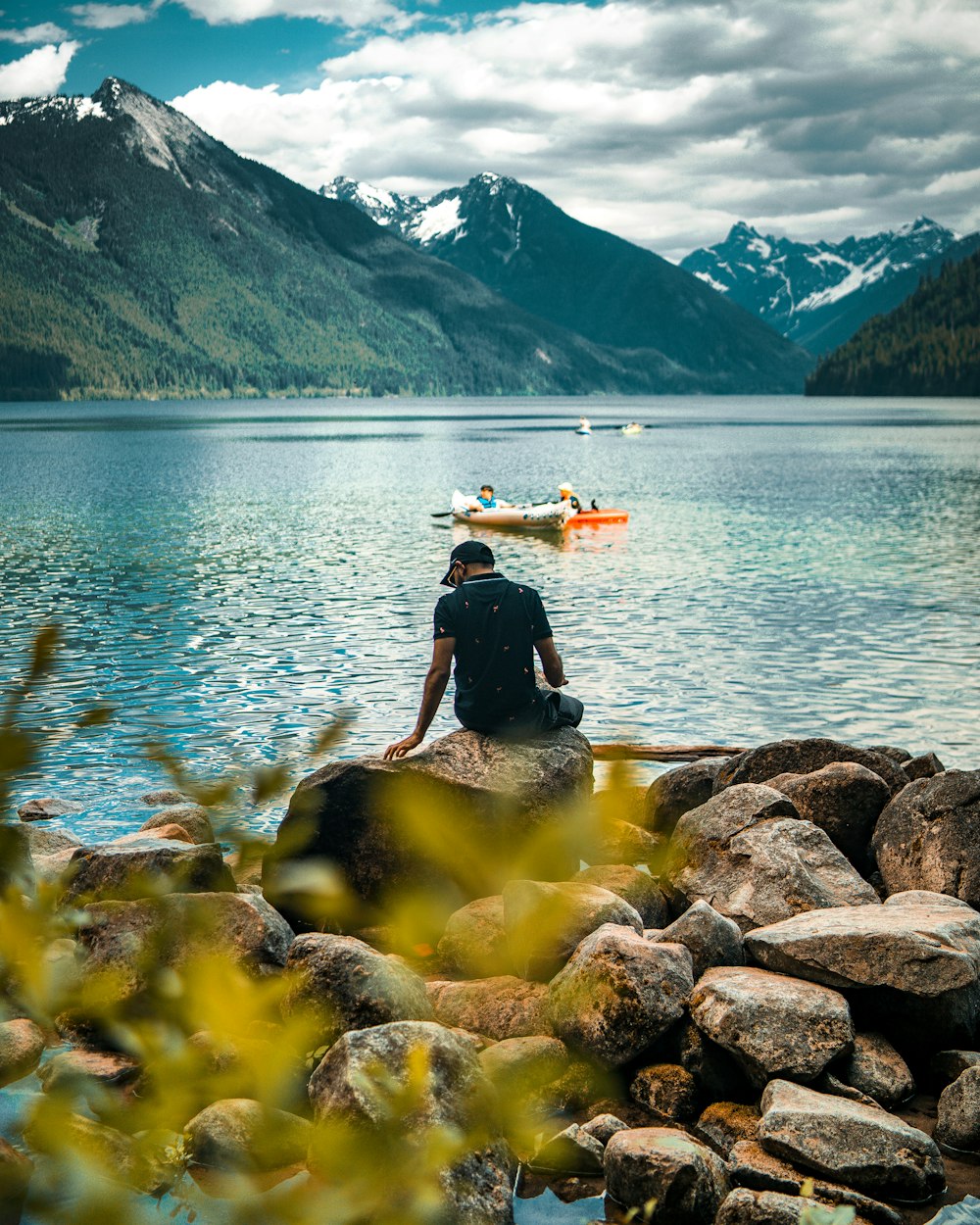 man in black shirt and black pants sitting on rock near body of water during daytime
