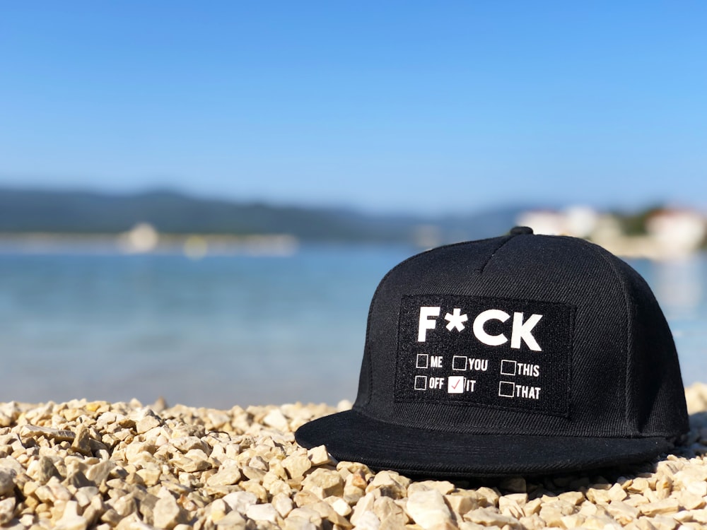 black and white fitted cap on brown rock near sea during daytime