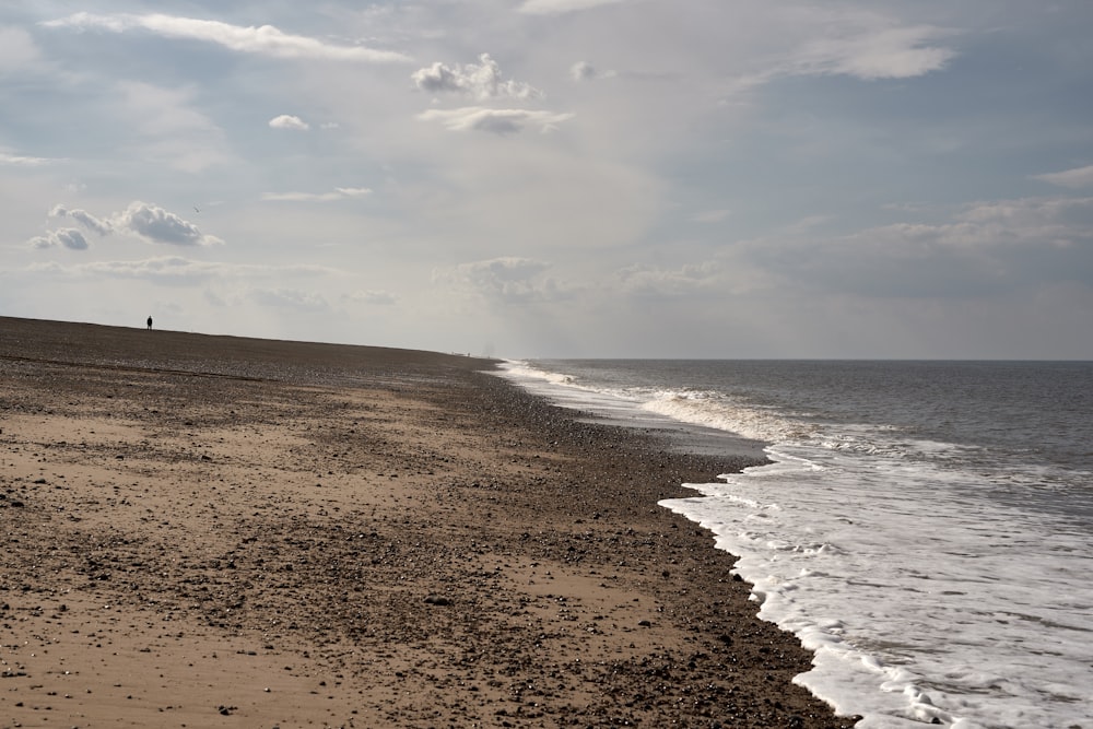 praia de areia marrom sob nuvens brancas durante o dia