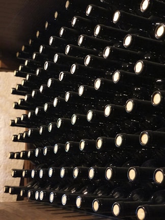 A neatly organized wine cellar with rows of wine bottles stored horizontally on wooden shelves. Each bottle is uniformly placed with corks facing outward, creating a visually appealing pattern. The cellar's ambient lighting casts a warm glow over the scene.
