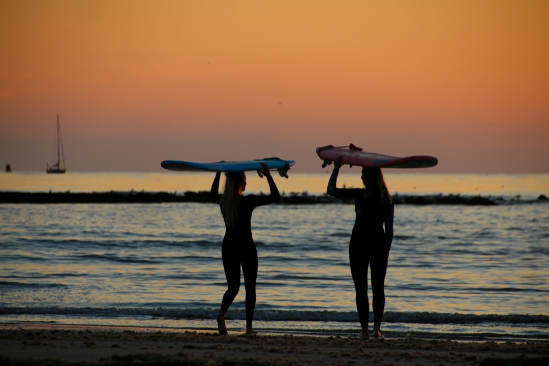 silhouette of 3 person holding surfboard on beach during sunset