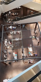 A multi-level indoor shopping mall with an open design and escalators visible. The image captures the bird's-eye view of various sections with organized displays of clothing and accessories. Shoppers are browsing through the store, creating a bustling yet organized atmosphere.