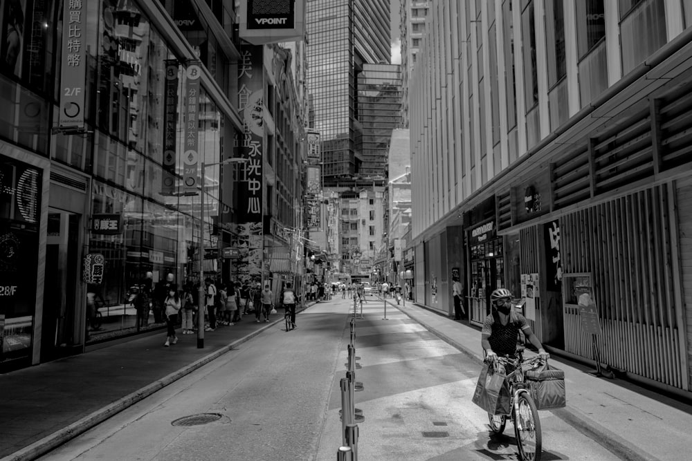 grayscale photo of people riding bicycle on road between high rise buildings