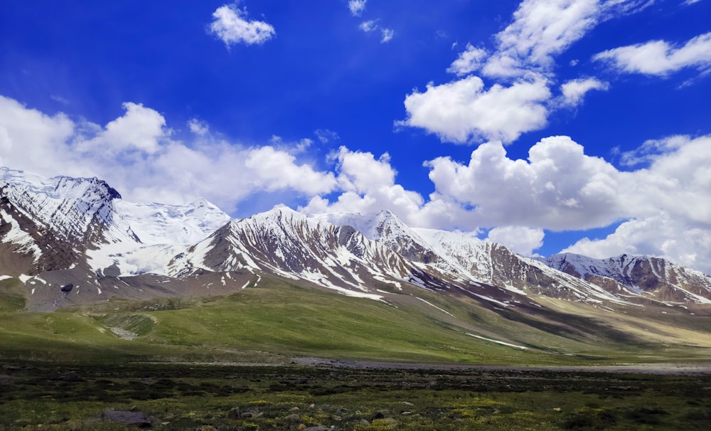 green grass field and mountain under blue sky and white clouds during daytime