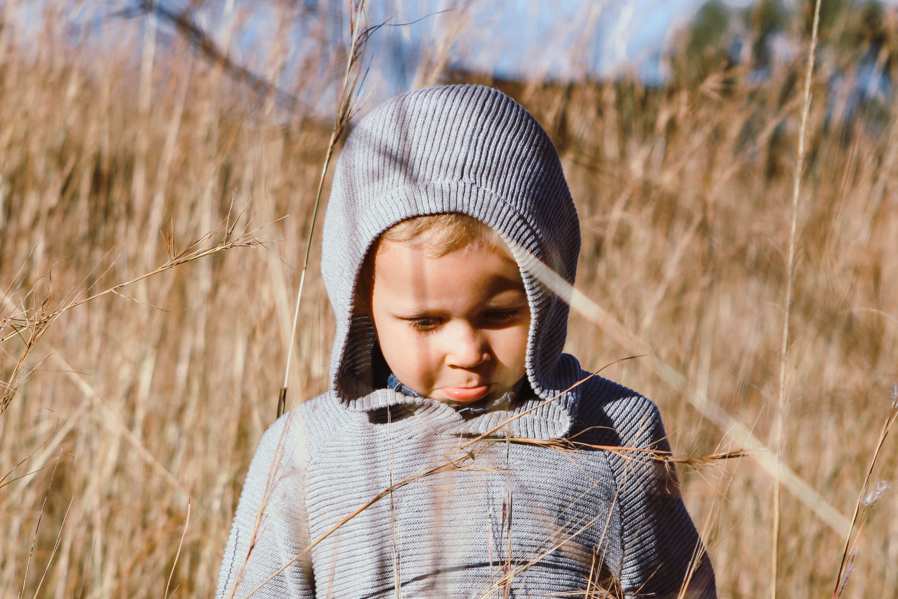 child in white and black hoodie standing on brown grass field during daytime