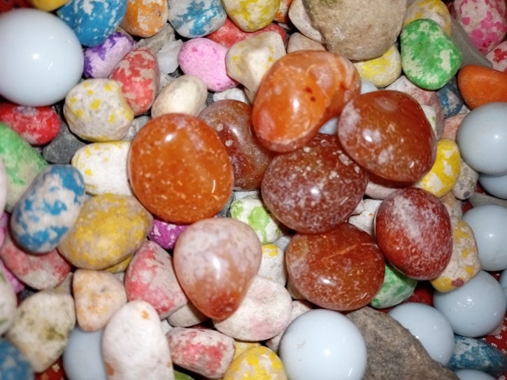A collection of smooth, colorful stones and pebbles in a variety of shapes and colors, including blue, orange, red, yellow, pink, and white.