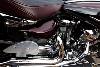 Close-up view of a motorcycle engine featuring chrome components and a burgundy leather seat. The metallic parts are polished with visible reflections, showcasing intricate mechanical details.