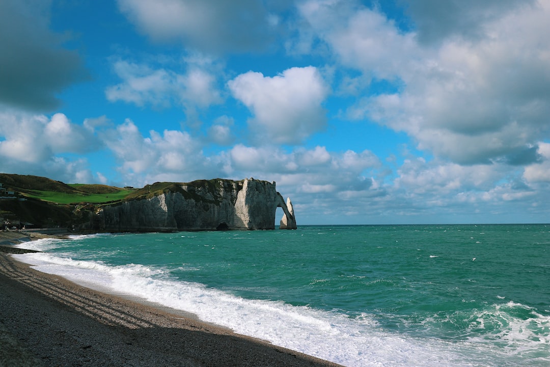 green and brown rock formation on sea under blue and white cloudy sky during daytime