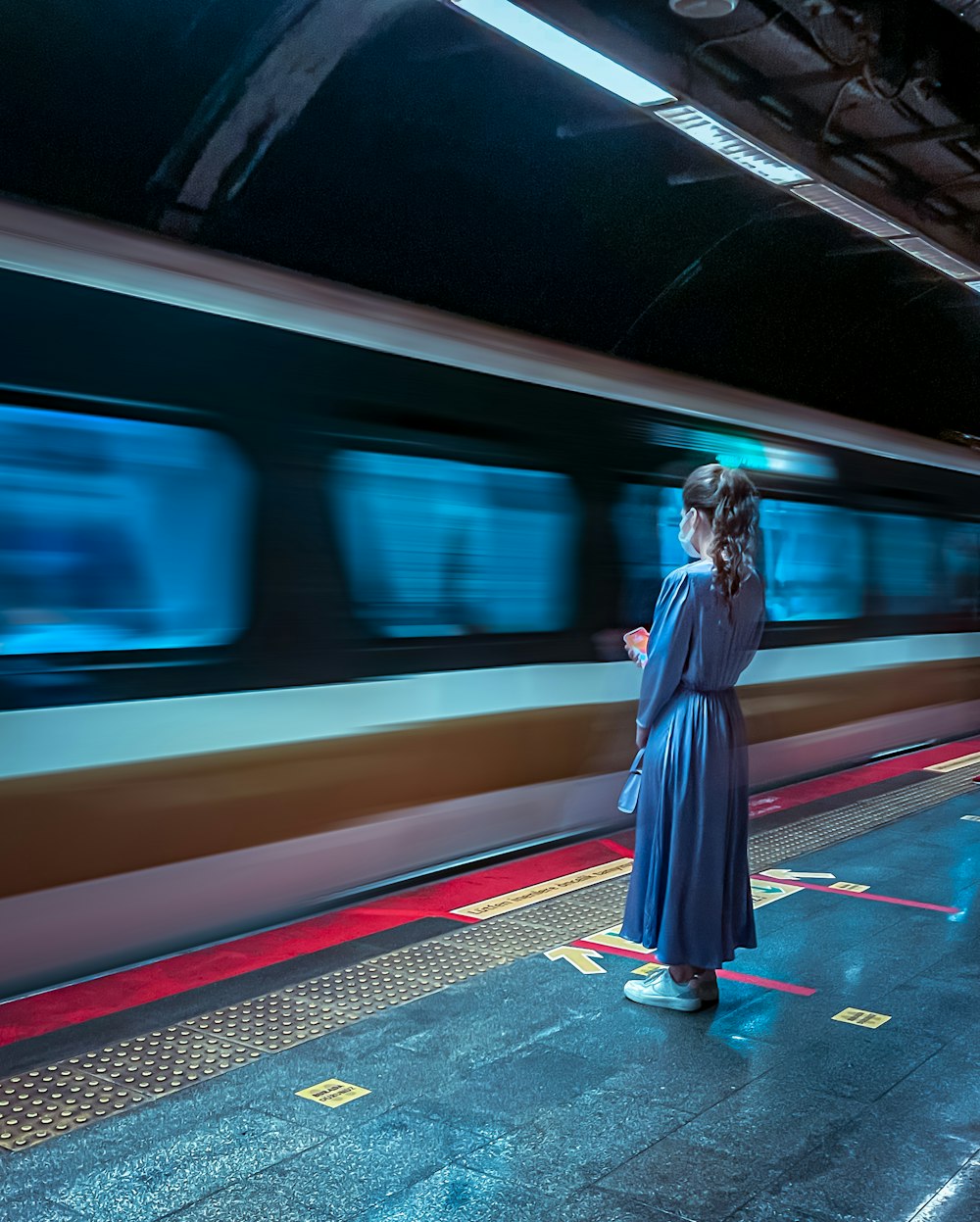 Mujer en vestido azul de manga larga de pie en la estación de tren