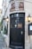 A charming entrance to a hotel and restaurant with a dark wooden door adorned with a decorative metal face. The entrance has a vintage sign above it reading 'Candlesticks Hotel and Restaurant.' Two traditional lanterns flank the door, providing a warm, inviting glow. Potted greenery lines the stone building, adding a touch of nature to the scene.