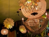 Elegant chandeliers with intricate designs hang from the ceiling, composed of delicate beads and petals that create a warm, inviting glow. The surroundings feature lush greenery and floral decorations that add a natural ambiance to the scene.