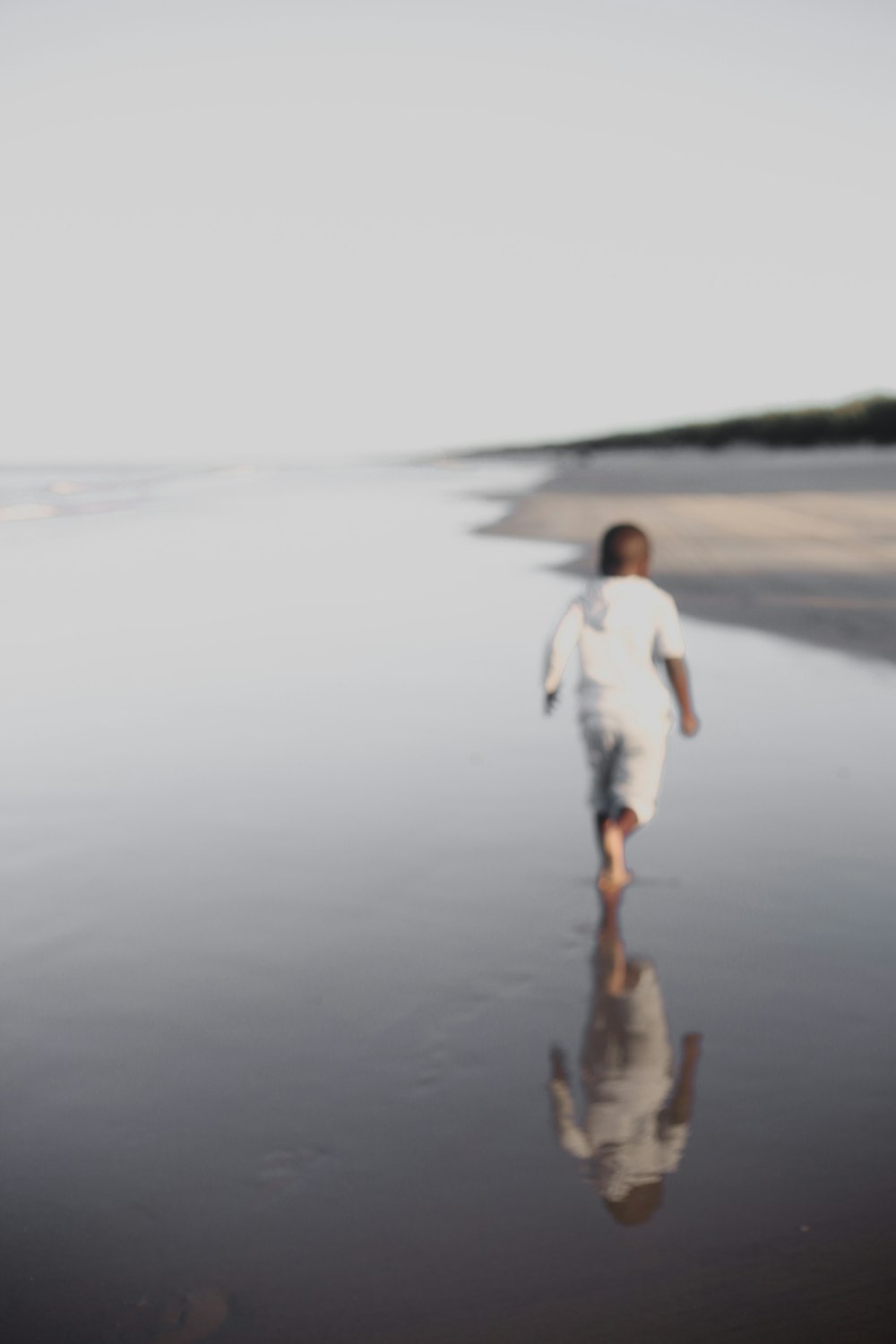 woman in white long sleeve shirt and white pants standing on brown sand during daytime