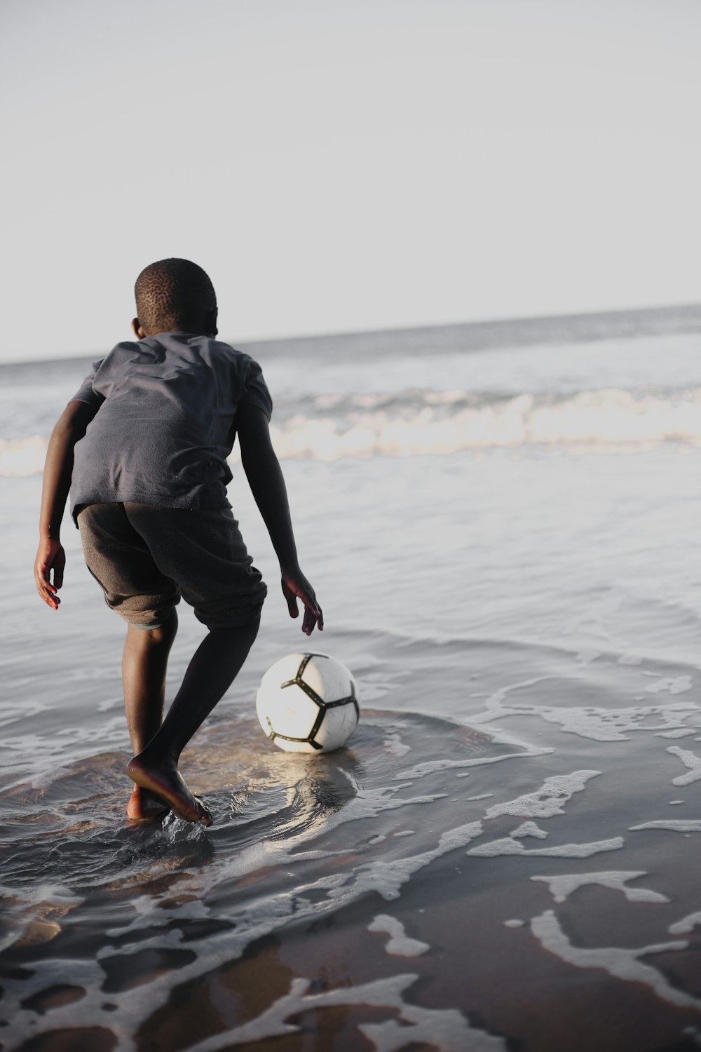 man in black shirt and black shorts playing soccer on beach during daytime