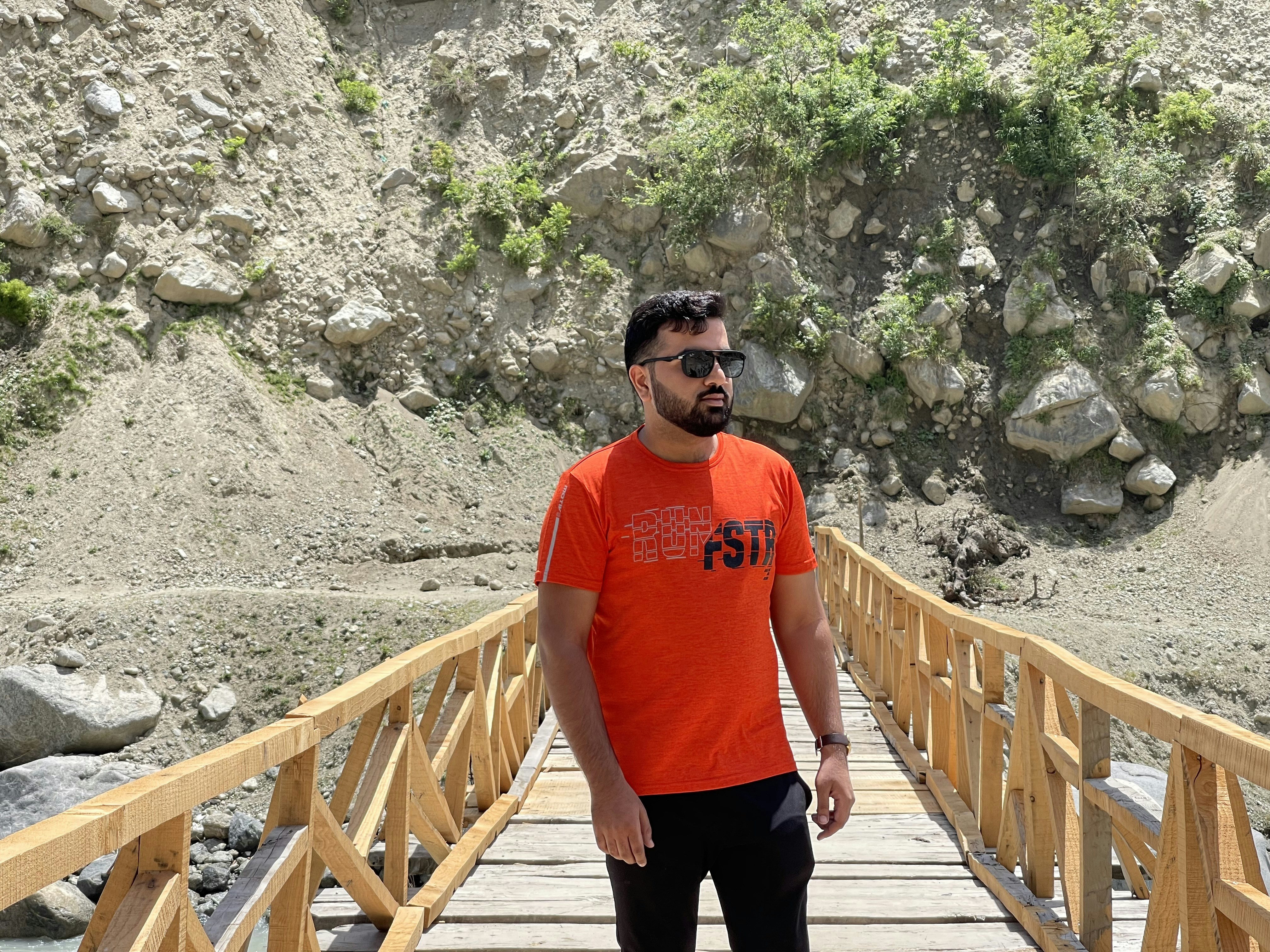 a man in an orange shirt standing on a wooden bridge