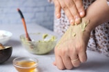 Hands gently mixing a creamy herbal face mask in a rustic ceramic bowl.