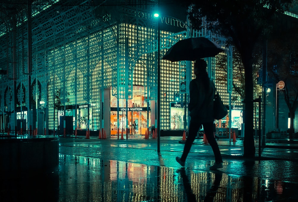 person holding umbrella standing on sidewalk during night time