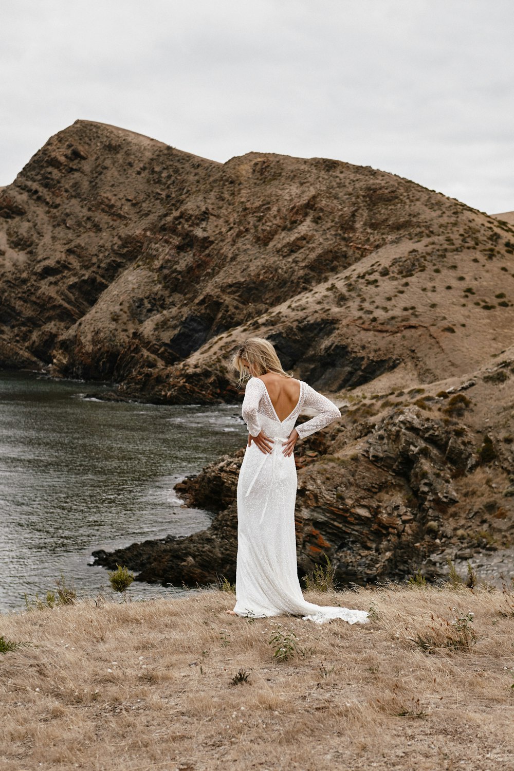 woman in white dress standing on brown rock near body of water during daytime