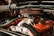 A detailed view of a car engine featuring a prominently visible air filter surrounded by various hoses and metal components. The engine has a bold Chevrolet logo and vibrant orange covers.