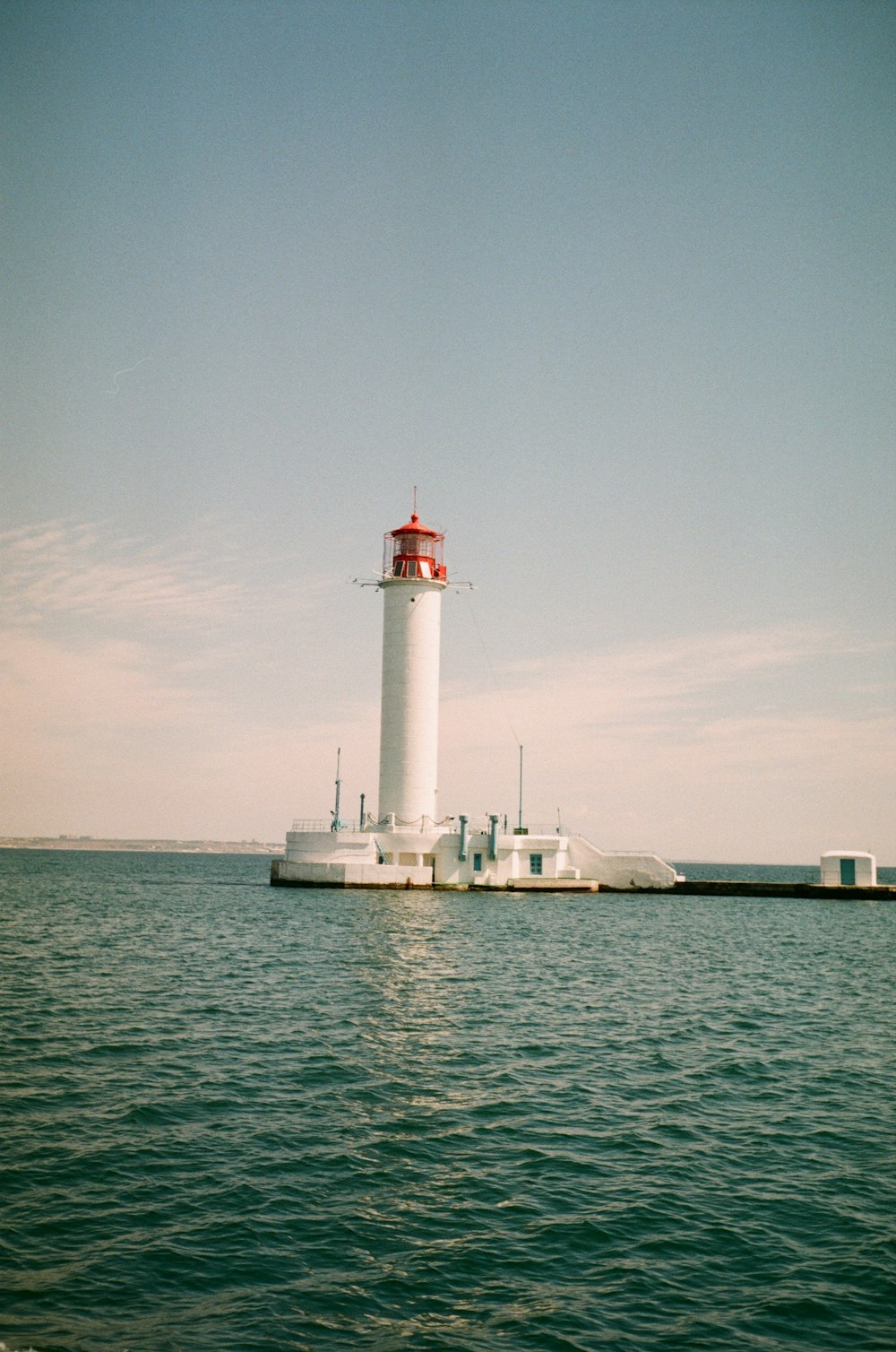white and red lighthouse on body of water under white clouds during daytime
