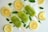 Three lime green popsicles are arranged on a bed of crushed ice, surrounded by lemon slices and fresh mint leaves. The setting suggests a refreshing summer treat, enhanced by the bright and vibrant color contrast between the green popsicles and the pale yellow lemons.