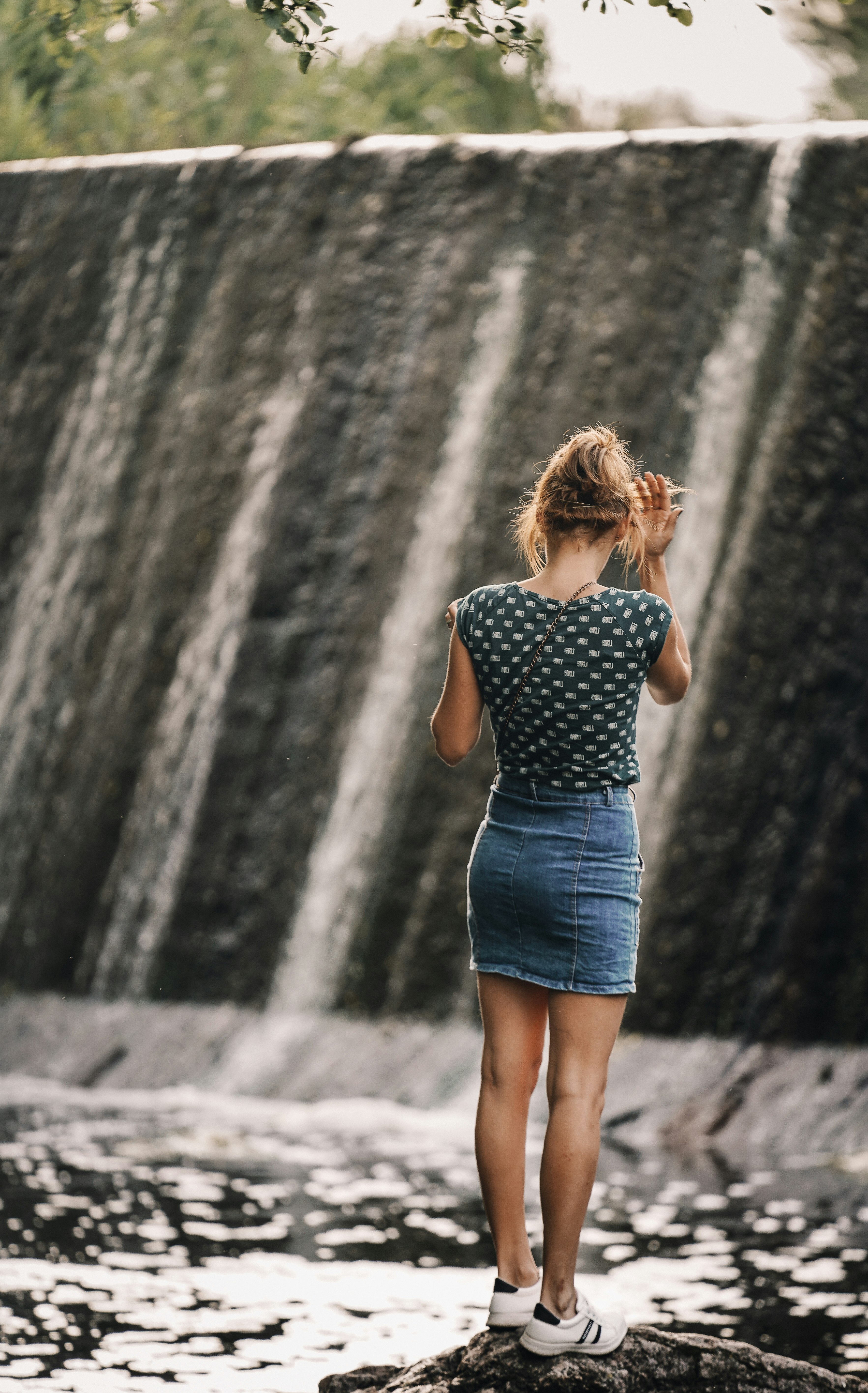 woman in blue and white polka dot dress standing in front of waterfalls during daytime